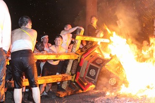 上半身が裸姿の男性が、神輿を火の中に入れている写真