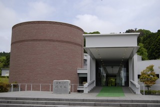茶色の円柱状の建物と横の白い建物の入り口が撮影された写真