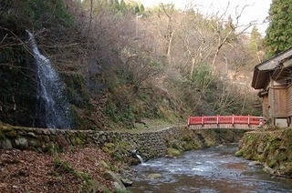 赤い手すりの橋の近くに滝が流れている写真
