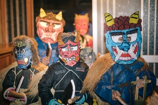 簑を着てお面をつけ鬼の扮した人たちが、家の玄関に集まっている写真