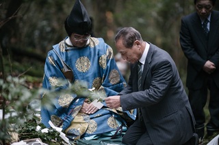 神主さんが見守る中、スーツを着た参拝者の1人が玉串を捧げている写真