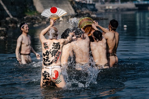 腰あたりまで水につかり、背中に「酒樽がえし」と書き、日の丸の扇子を広げたふんどし姿の男性の前で、他のふんどし姿の男性たちが樽を取り合っている写真