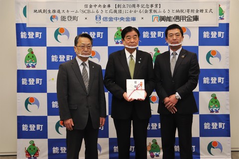 能登町のバックボードの前で、目録を持った関係者を中心にスーツ姿の市長と関係者の1名で記念撮影している写真