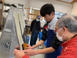生徒が保存会の方に教わりながら刷毛を片手に持ち紙漉き体験を行っている様子の写真