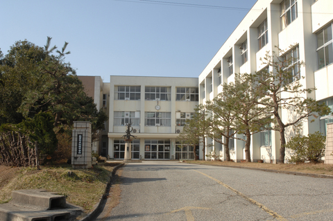 白い外壁で3階建てのL字型の校舎と手入れされた植栽が植えられた中学校の外観写真