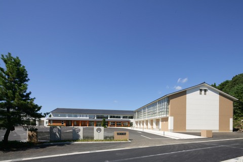 入り口入って右側に体育館、その奥に2階建ての校舎が建っており広々とした駐車場がある中学校の外観写真