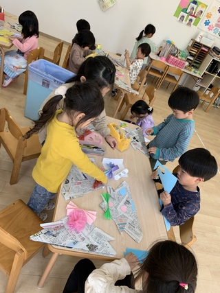 新聞紙で作った兜の帽子にカラフルな折り紙や画用紙で飾り付けをしている園児たちの写真