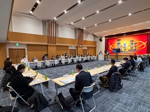 ステージ前に演台が設置されその手前に長テーブルをコの字型に設置した会場に複数名の関係者が着席をしている委員会の様子の写真