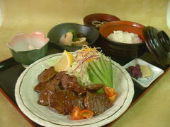折敷に小鉢、ご飯、吸い物、漬物、野菜ときゅうりが添えられた牛焼き肉定食の写真