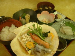 折敷に小鉢、ご飯、吸い物、漬物、大きなホタテの貝に海鮮が盛られたいしり貝焼き定食の写真