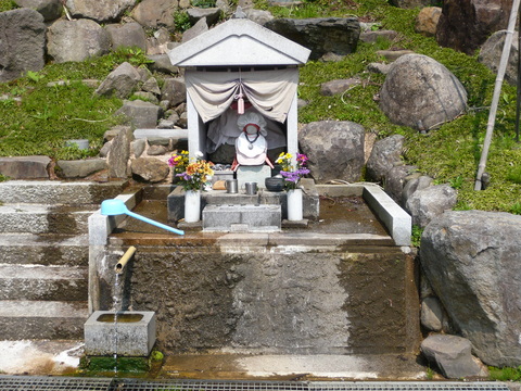 石造の土台の正面から水が流れ出ており、土台の上にいぼ地蔵の祠堂がある写真