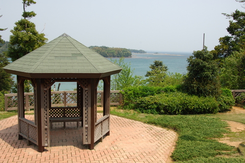 広がる海を背景に能登内浦の高台にある円錐型屋根でベンチがある休憩所の写真