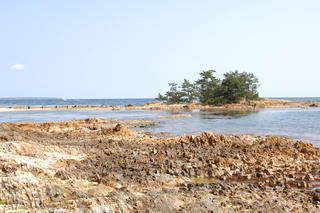 多くの部分が侵食された茶色の岩の奥にに小さな島が見えている写真