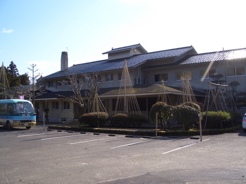 手前に駐車場があり、植木が植栽された庭の奥に国民宿舎能登うしつ荘のある建物の外観写真
