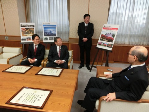 資料を見せながら説明している持木町長と椅子に腰かけて話を聞いている、谷本知事と二人の男性の写真