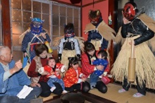 蓑を付けフカグツを履き、竹で作った筒のようなものをさげた鬼たちが子供の近くに集まる様子の写真