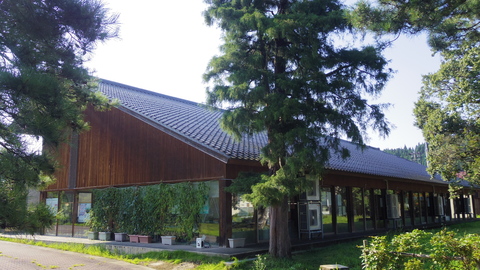 建物の近くに背の高い木が数本立ち、木の外壁とガラス窓の柳田教養文化館の写真