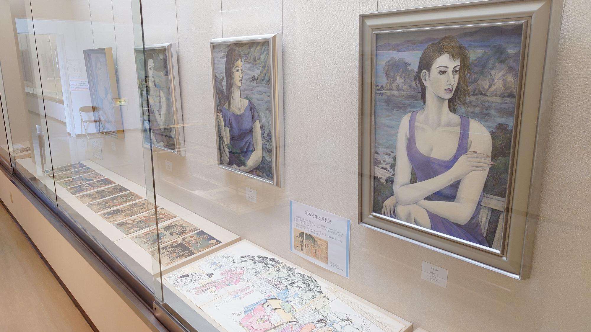 額に入った作品がガラスケースに展示されている1階展示室の写真