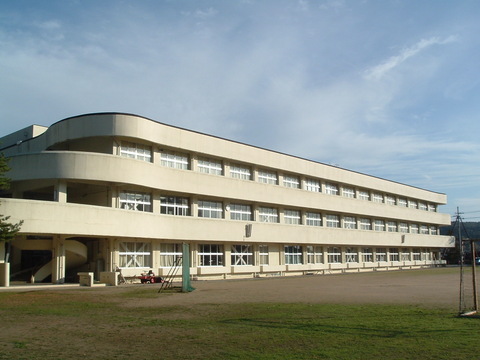 白い外壁で3階建ての校舎と広々とした校庭がある宇出津小学校の外観写真