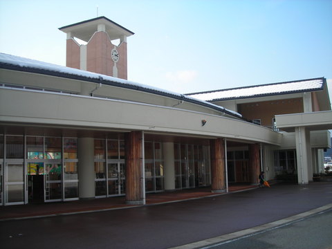 1階建ての校舎で屋根に時計台があり、雪が薄く積もっている小学校の外観写真