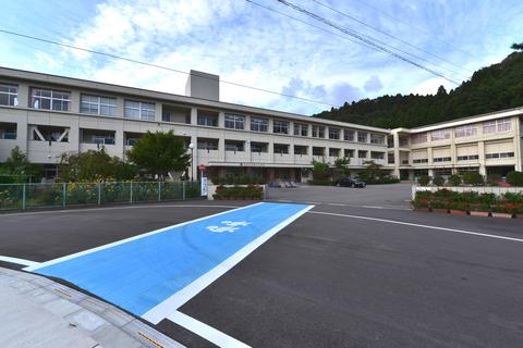 白い外壁で3階建てのL字型の校舎を、校門入り口につながる横断歩道の道路を挟んだ向かい側から撮影した写真