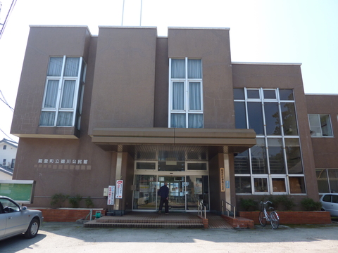 茶色い外壁で2階建て、大きなガラス窓が設置されている建物の外観写真