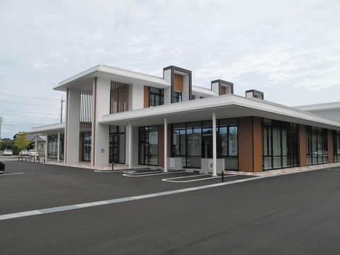 白を基調とした建物で壁は大きなガラス窓、入口横に屋根付きの駐車場がある建物の外観写真